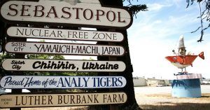 The Welcome to Sebastopol sign with fun facts about the town such as its sister cities and local high school sports team. In the background is sculpture art of an orange shark and clown fisherman that is popular in the area.